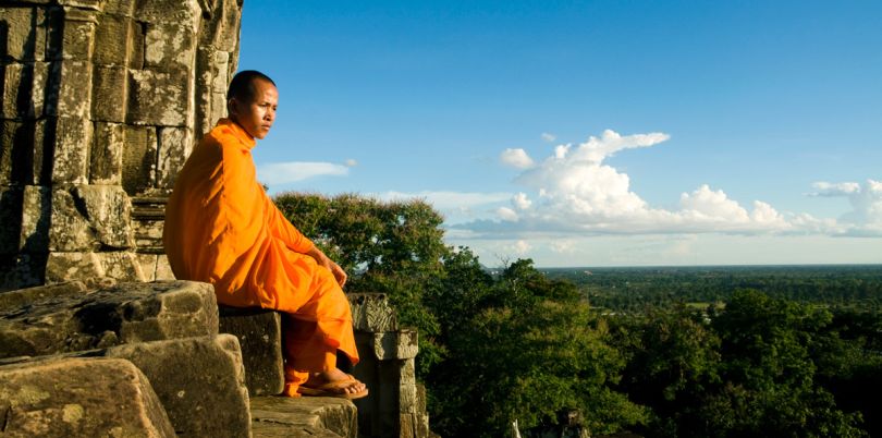 Monk sitting on a rock overlooking the abyss in Bayon, Cambodia