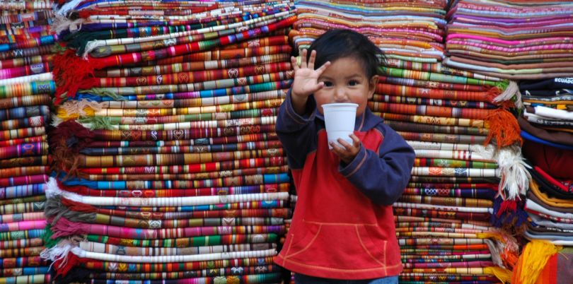 Little child with cup standing in front of textiles in Ecuador