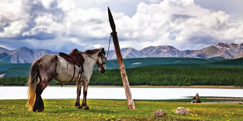 Horse overlooking its rider by a lake, Mongolia