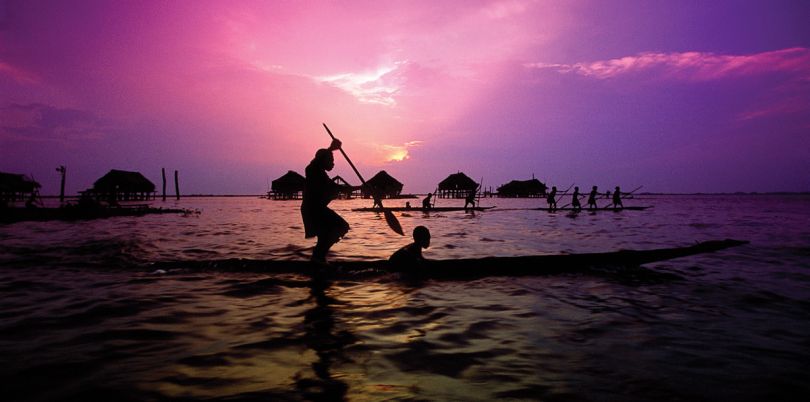 Rowers in a boat sailing around houses on stilts at dawn in Papua New Guinea